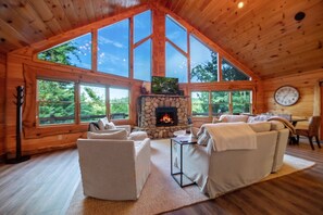 A spacious living room with a stone fireplace, large windows, and wooden ceiling. - Luxury Mountain View Cabin with Jacuzzi (Blue Ridge)