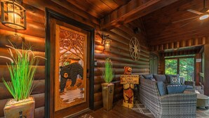 Ein Blockhaus-Interieur mit einer Holztür, einer Bärenskulptur, einem Willkommensschild und einer gemütlichen Sitzecke mit Blick ins Freie.
