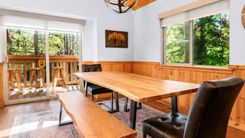 A wooden dining table with benches, a chandelier, and a view of the outdoors.