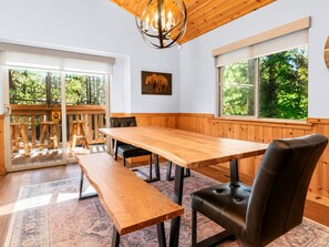 A wooden dining table with benches, a chandelier, and a view of the outdoors.