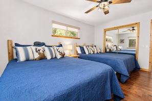 Ein Zimmer mit zwei Betten, jeweils mit blauer Bettwäsche und dekorativen Kissen, einem Deckenventilator und einem großen Spiegel.