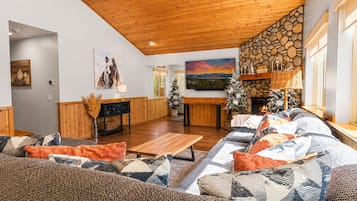 A cozy living room with a wooden ceiling, a stone fireplace, and a large sofa with patterned cushions.