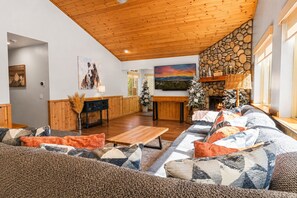 A cozy living room with a wooden ceiling, a stone fireplace, and a large sofa with patterned cushions.