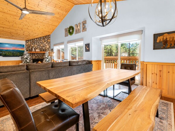 A cozy interior with a wooden ceiling, a stone wall, a fireplace, a large window, and a dining area with benches.