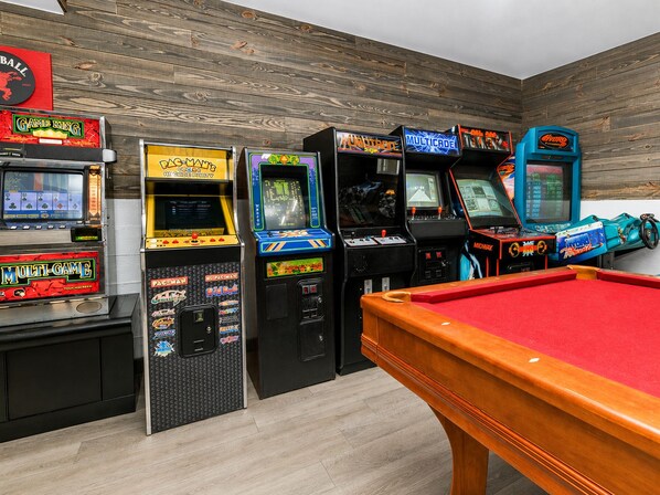 A pool table with arcade machines in a room with wooden walls.