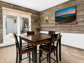Ein Essbereich mit einem Holztisch und Stühlen, einem an der Wand befestigten Fernseher und einem schönen Ausblick.