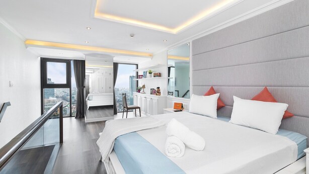 A modern hotel room with a large bed, a city view, a balcony, and a desk with a chair. - Luxury loft penthouse @ Ben Thanh Tower (hồ chí minh)