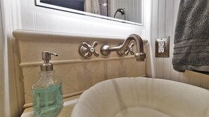 Une salle de bain avec une baignoire beige, un robinet argenté avec un réglage pour l’eau chaude et l’eau froide, et un distributeur de savon en verre.