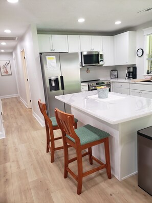 A modern kitchen with white cabinets, stainless steel appliances, and a central island with two wooden chairs. - All Newly remodeled-- stylish luxury nestled in rural neighborhood - Forest View (Stanton)