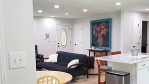 A modern living room with a black sofa, a wooden dining table, and a kitchen area with a stainless steel refrigerator. - All Newly remodeled-- stylish luxury nestled in rural neighborhood - Forest View (Stanton)