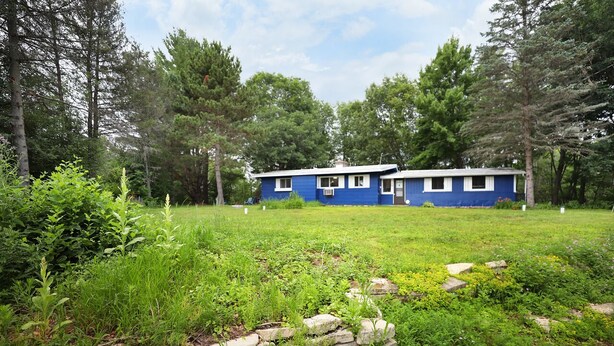 Une maison bleue à deux étages, avec un mur de pierre en premier plan.