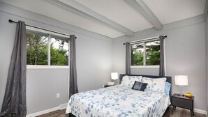 A bedroom with a bed, two bedside tables with lamps, and large windows with curtains. - Beautiful 2-bedroom Cottage (Waupaca)