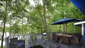 A deck with wicker furniture, a grill, and a view of a lake surrounded by trees. - Beautiful 2-bedroom Cottage (Waupaca)