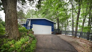 A blue garage with a white door, surrounded by trees and a wooden fence. - Beautiful 2-bedroom Cottage (Waupaca)