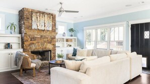 A living room with a stone fireplace, a large window, and a sofa. - Luxury 6-Bedroom Home in Prime Decatur Neighborhood, Near DT ATL (Decatur)