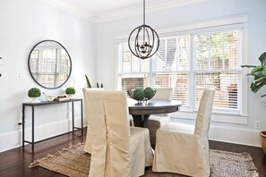 A dining area with a round table, two chairs, a black pendant light, a round mirror, and a window with blinds. - Luxury 6-Bedroom Home in Prime Decatur Neighborhood, Near DT ATL (Decatur)