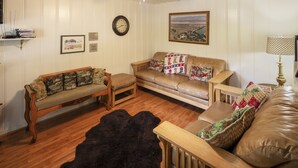A living room with two sofas, a wooden coffee table, a black furry rug, a ceiling fan, a wall clock, and a framed landscape painting.