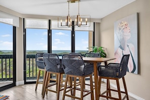 A dining area with a table and chairs, large windows with a view, and a chandelier.