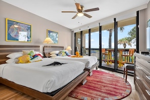 A bedroom with two beds, a ceiling fan, and a balcony with outdoor furniture.