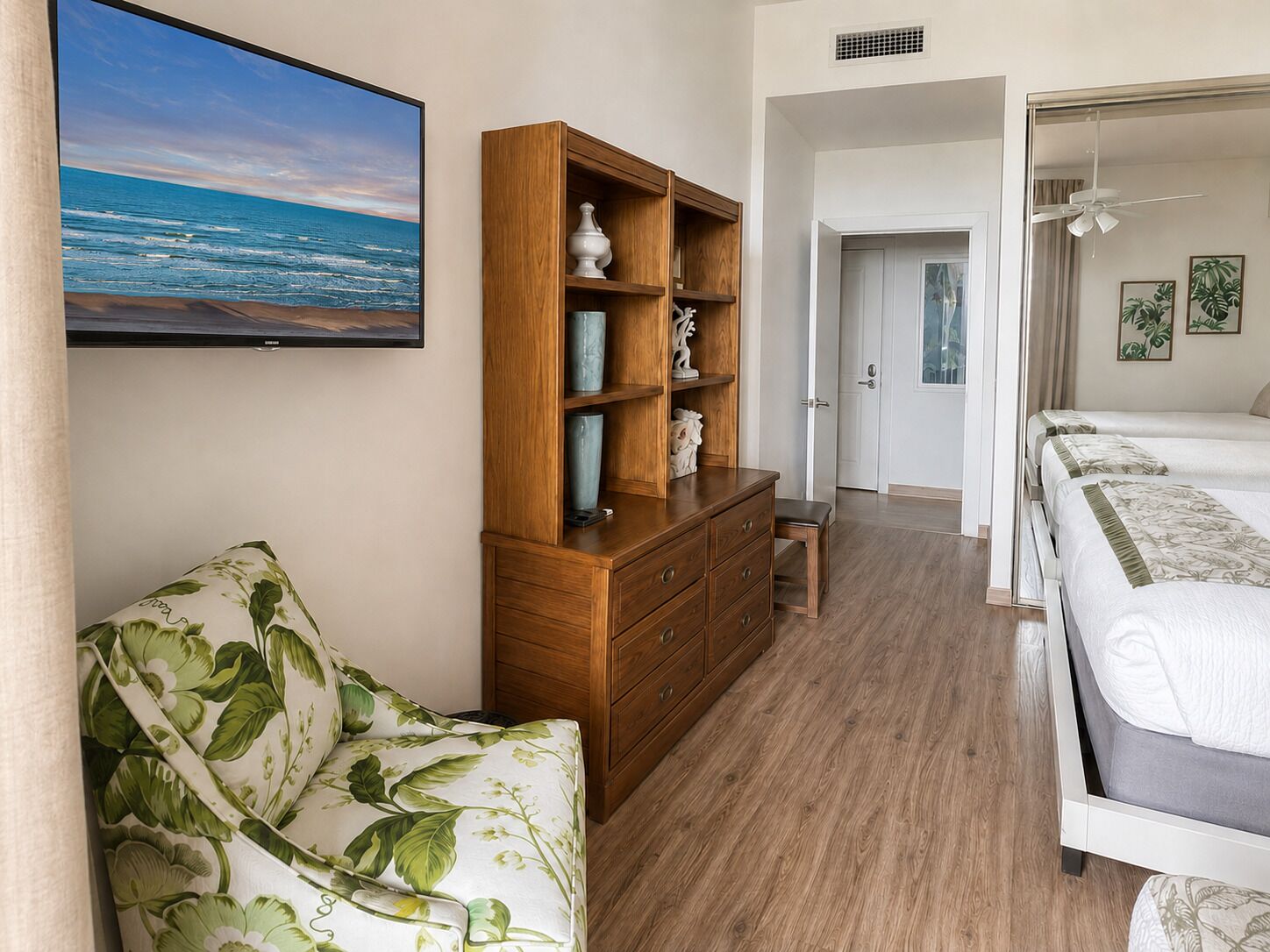 Un dormitorio con un armario de madera, un sofá, una cama y un televisor que muestra una escena de playa.