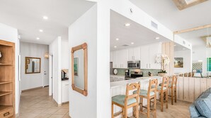 A modern kitchen with white cabinets, a wooden bar counter, and a seating area with wooden chairs. - Sandpiper Condominiums 1206, Panoramic Gulf Views w/ direct access to Mustang Island/Port A beaches. (Port Aransas)