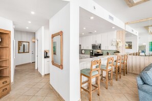 Una cocina moderna con armarios blancos, una barra de madera y una zona de estar con sillas de madera.