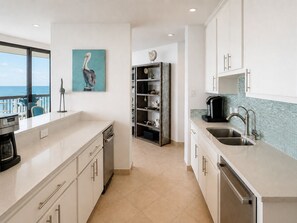 A modern kitchen with white cabinetry, a coffee machine, and a view of the ocean.