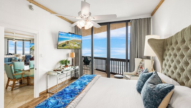 A bedroom with a large bed, a ceiling fan, a TV, and a balcony with a view. - Sandpiper Condominiums 1206, Panoramic Gulf Views w/ direct access to Mustang Island/Port A beaches. (Port Aransas)