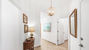 A hallway with a wooden console table, a lamp, framed artwork, and a door with a mirror. - Sandpiper Condominiums 1206, Panoramic Gulf Views w/ direct access to Mustang Island/Port A beaches. (Port Aransas)