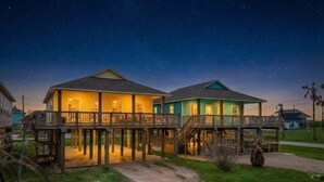 Deux maisons situées en bord de mer, dotées de terrasses en bois, et un ciel nocturne dégagé.