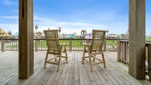Une terrasse en bois avec deux chaises en bois et une table, donnant sur une zone herbeuse avec des bâtiments en arrière-plan.