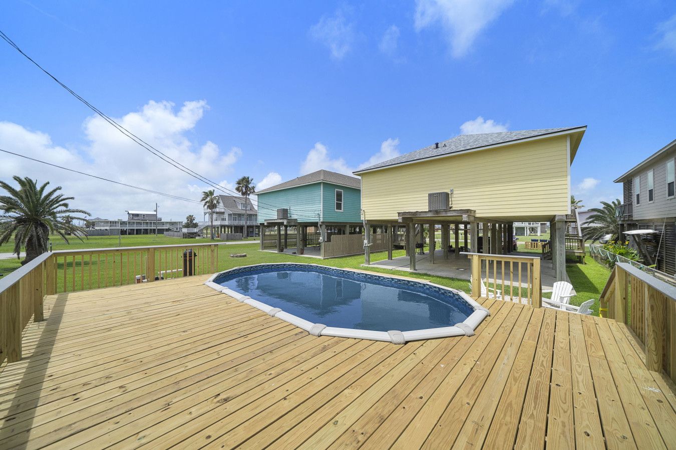 Una terraza de madera con piscina, un porche cubierto y un patio trasero cercado.