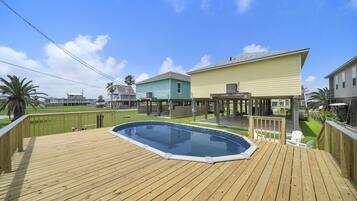 Una terraza de madera con piscina, un porche cubierto y un patio trasero cercado.