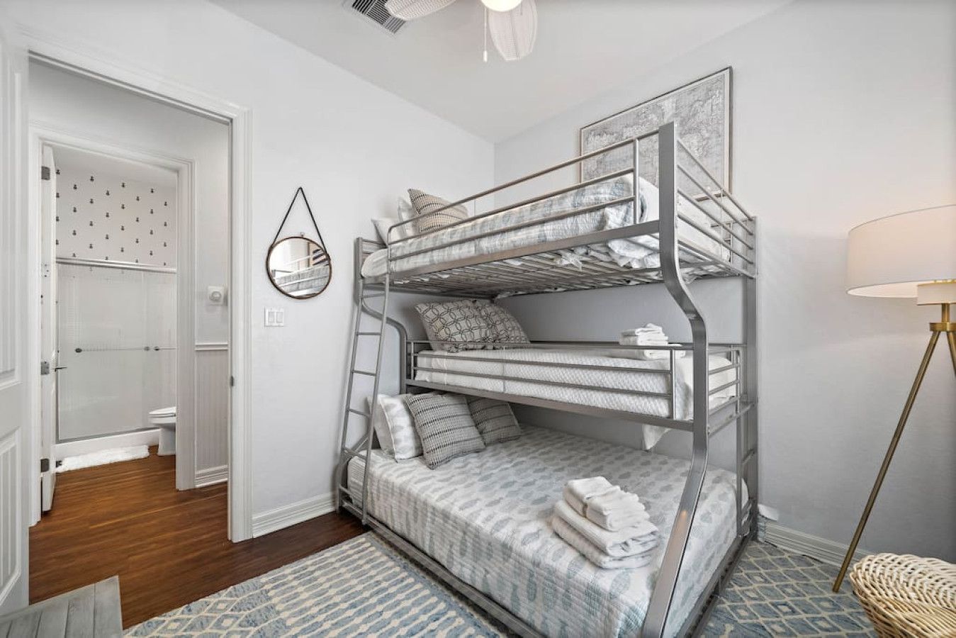 A bunk bed room with a mirror, a lamp, and a door leading to a bathroom.