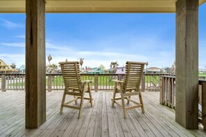 Een houten terras met twee houten stoelen en een tafel, met uitzicht op een gazon met gebouwen op de achtergrond.