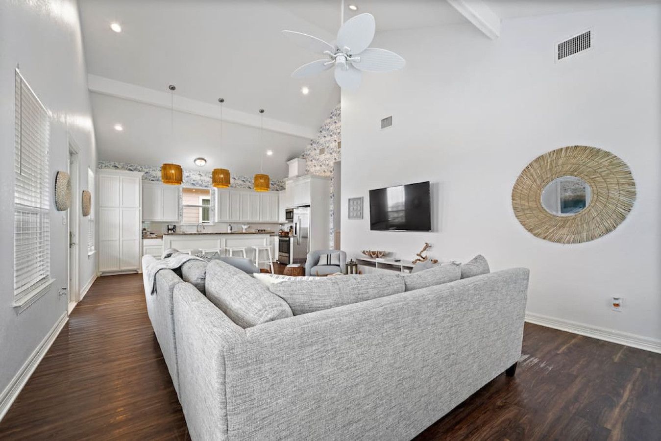 A modern living room with a grey sectional sofa, a flat-screen TV mounted on the wall, and a decorative mirror.