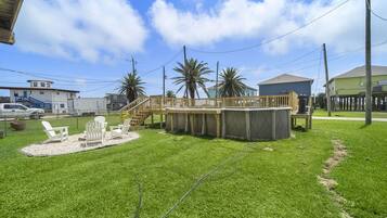 A backyard with a wooden deck, outdoor seating, and a swimming pool.