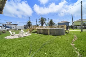 A backyard with a wooden deck, outdoor seating, and a swimming pool.