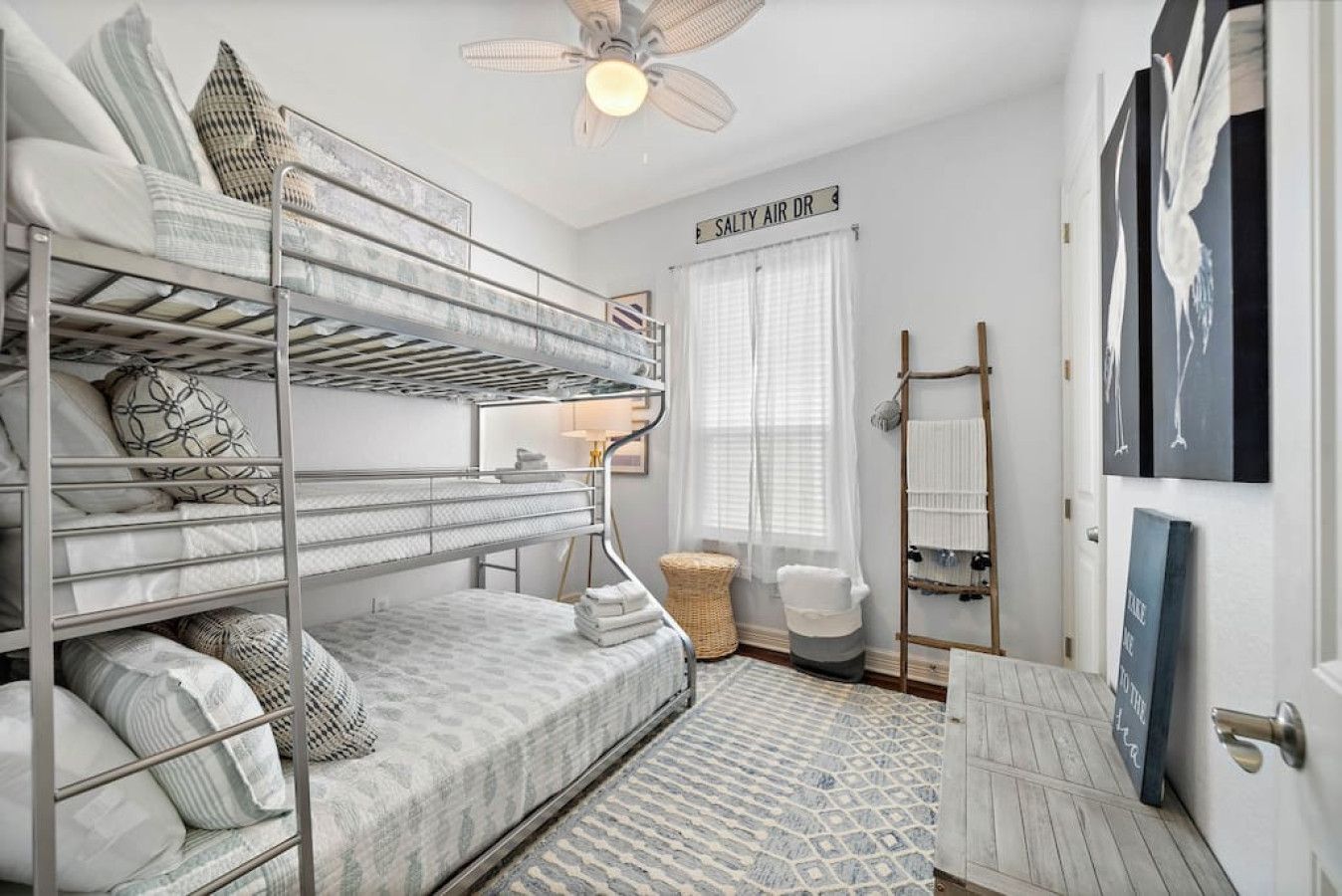 A bunk bed room with a ceiling fan, a sign reading "SALTY AIR DR", and a ladder for hanging clothes.