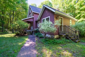 Situated in a wooded area, this charming home offers a serene and secluded environment with a well-maintained lawn and lush greenery.