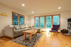 Relax in a serene space with a large sectional sofa, coffee table, and armchair, surrounded by a forest view.