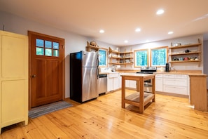 Kitchen features a central island, cabinetry, and shelving, along with a refrigerator and oven.