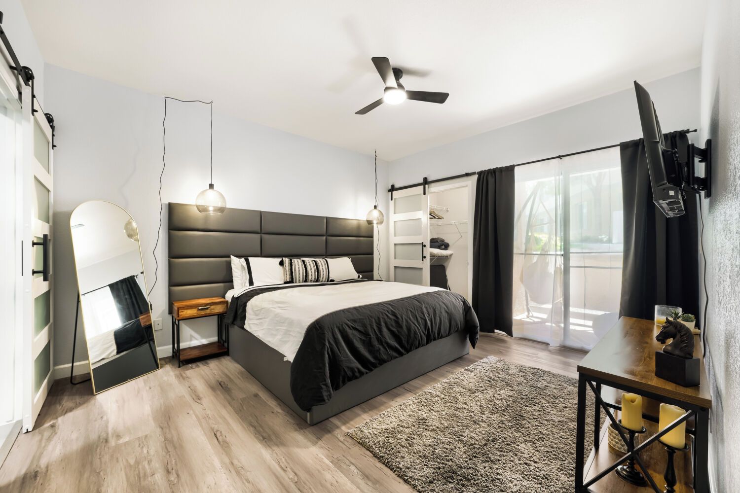 A modern bedroom with a bed, bedside tables, a ceiling fan, and a large window with curtains.