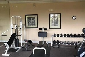 A gym with exercise equipment, including a bench press, dumbbells, and a bike frame.