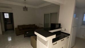 Et moderne køkken med hvide skabe og en sort bordplade. I det tilstødende opholdsområde er der en brun sofa.