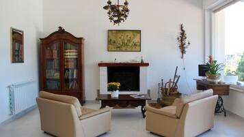 A living room with two beige sofas, a wooden bookcase, a fireplace, a chandelier, and a window with a view.