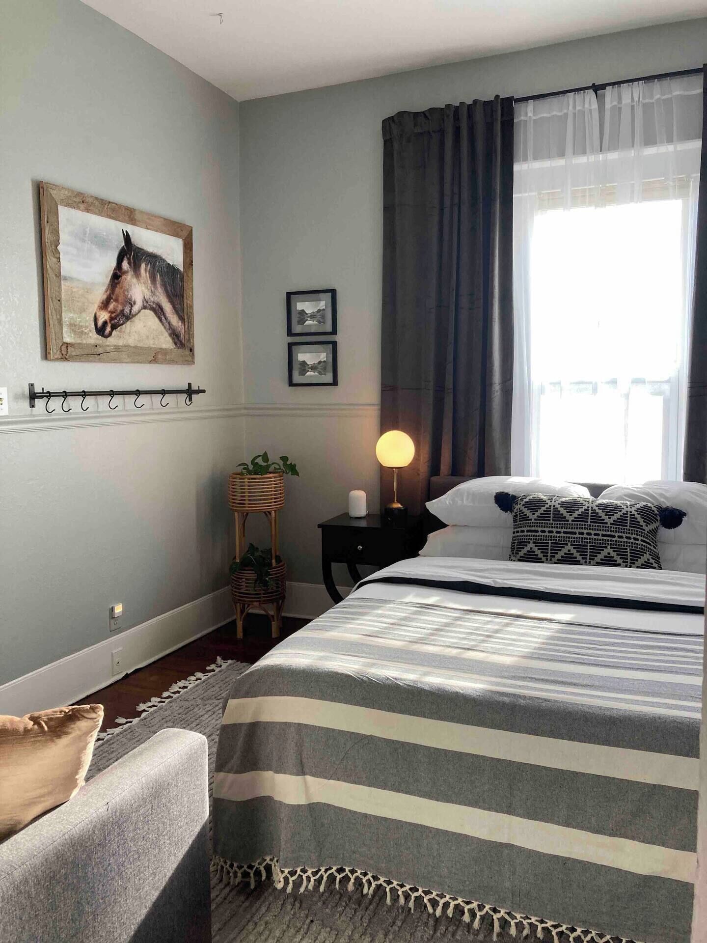 Une chambre à coucher avec un lit, une table de chevet avec une lampe, une étagère murale ornée de plantes et une fenêtre avec des rideaux.