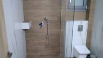 A small, enclosed shower area with a glass door, a white toilet, and a wooden wall.