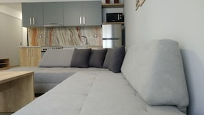 A modern living room with a grey sectional sofa, a wooden coffee table, and a kitchen area with grey cabinets and a built-in microwave.