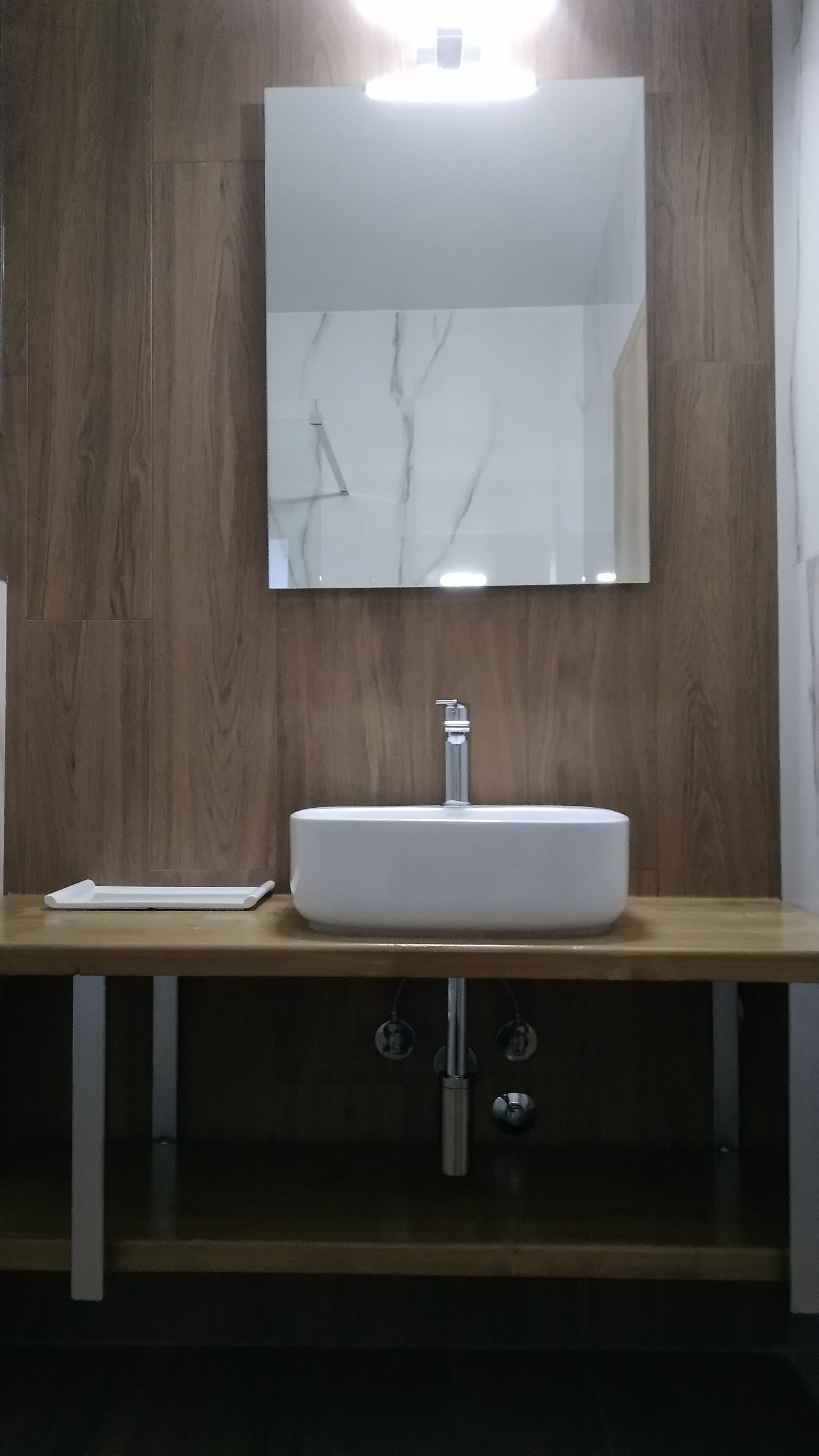 Un baño con tocador de madera, un lavabo blanco y un espejo.